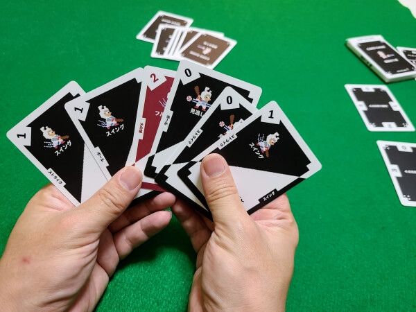 Player holding up a hand of physical cards. In the background are more cards spread out on the table.